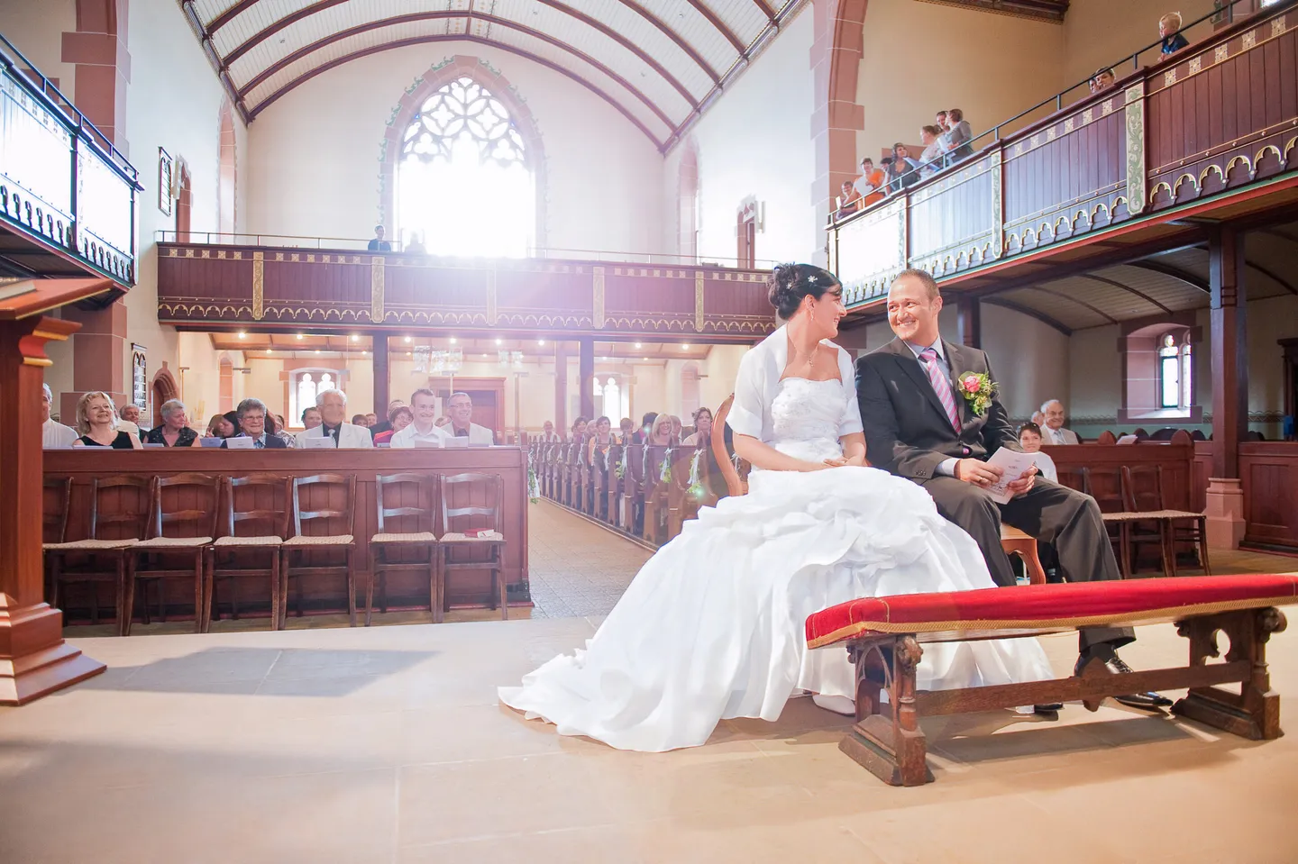 Bride and groom smiling in church with guests in the background.