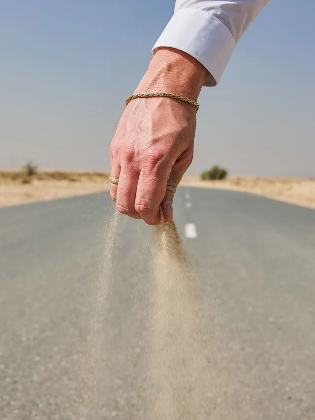 Hand streut Sand auf Straße in Wüste