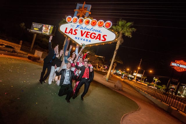 Group celebrating in front of Las Vegas sign at night.