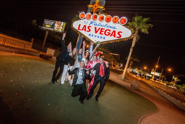 Group celebrating in front of Las Vegas sign at night.