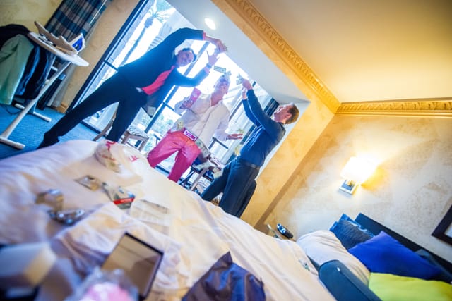 Three people celebrate with money in a hotel room.