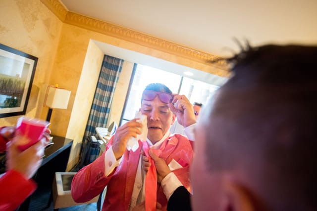 Man crying in pink suit, glasses in hand.