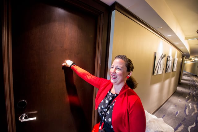 Woman knocks on door in hotel corridor.